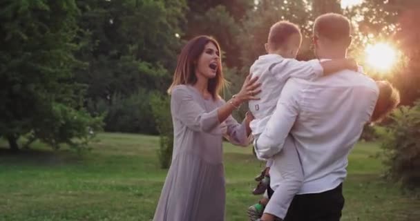 Große Familie zwei Kinder und junge Eltern in lässiger Kleidung genießen die gemeinsame Zeit inmitten eines grünen Parks — Stockvideo