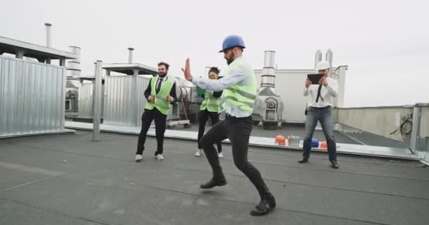 Um homem de arquitetura fina com óculos e uma barba danças modernas na frente de seus amigos trabalhadores que são todos também arquitetos, ao ser filmado por um cara bonito que está vestindo uma camisa e um — Vídeo de Stock