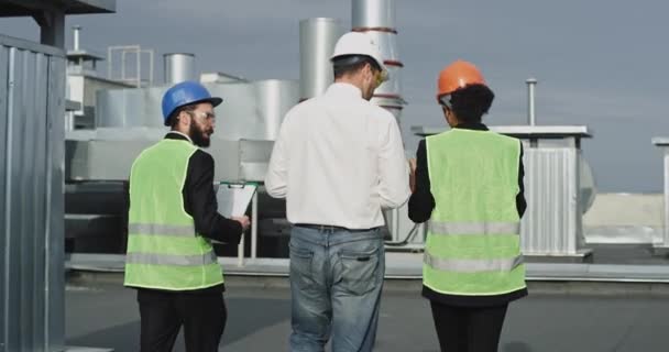 Três trabalhadores da construção caminham em frente enquanto discutem algo entre eles, há uma mulher que é de altura média e um homem no meio que é alto, finalmente, um cara menor que também anda — Vídeo de Stock