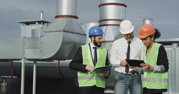 Both of the construction workers are showing the architect in the middle, he is good looking and he is dressed differently to the two workers which make him stand out, the two workers discuss the — стоковое видео