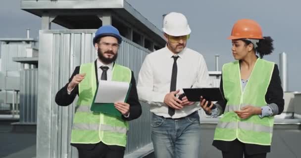 Il giovane indica un punto di vista per l'architetto spiega a lui, e la giovane donna di costruzione è d'accordo con loro manca la testa, i due operai edili sia indossare una giacca gialla al neon e — Video Stock