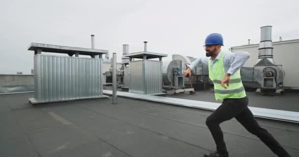 Auf dem Dach der Baustelle charismatischer Ingenieur tanzt und genießt den Moment, während er die Ration hält und auf den Architekten wartet — Stockvideo