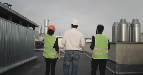 The two fit looking construction workers wearing bright eye catching yellow jackets are accompanying an architect in the middle who is a bit large and is wearing a white shirt, they walk to a desk — стоковое видео