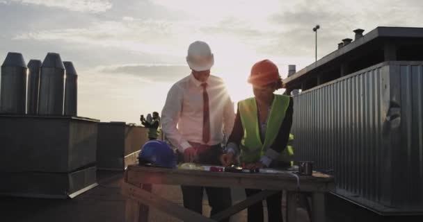 El admirable arquitecto gordito trabaja con la encantadora joven en los estampados azules para un sitio de construcción — Vídeos de Stock