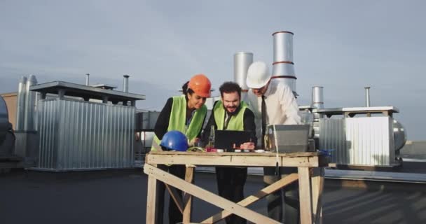 Três trabalhadores da construção civil estão em torno de uma mesa com um iPad nele, todos eles se parecem com o seu salto com alegria e sobre a lua com emoção, há dois construtores que k estão vestindo laranja — Vídeo de Stock