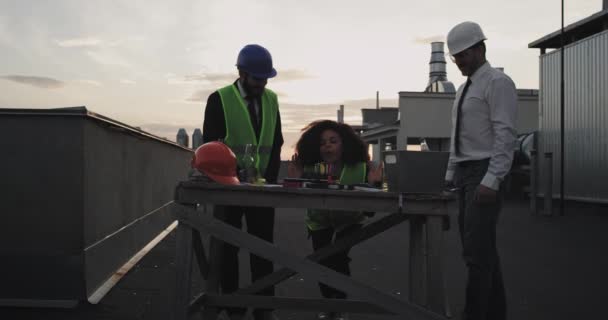 En la azotea del sitio de construcción dos arquitectos y una mujer ingeniera celebrando la fiesta de cumpleaños en la azotea del sitio de construcción señora africana soplando las velas — Vídeos de Stock