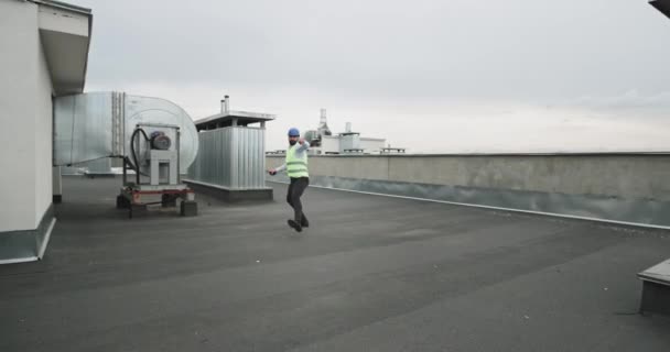 Er springt und bewegt sich charismatisch vor dem Kameramann auf der Baustelle und lächelt groß aufgeregt, er trägt einen Helm — Stockvideo