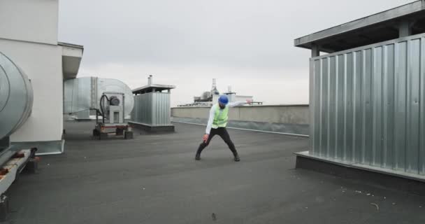No canteiro de obras no telhado do edifício arquiteto carismático ou engenheiro dançando na frente da câmera enquanto vestindo um capacete de equipamento de segurança e roupas de negócios — Vídeo de Stock