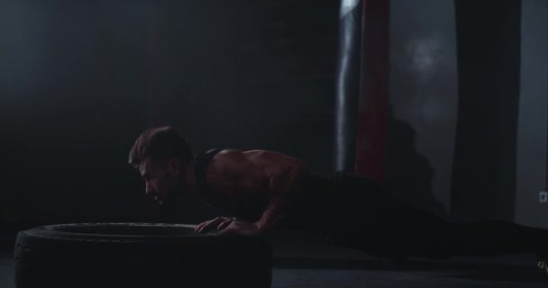 Fitter muskulöser Mann, der Crossfit-Übungen macht, Liegestütze über einen großen Gummireifen in einer Turnstunde macht, er schwitzt sehr konzentriert und arbeitet intensiv — Stockvideo