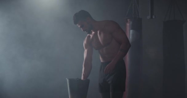 Charismatische kerel met een baard en tatoeages zet wat poeder op zijn handen voordat hij zijn trainingsoefeningen in een gymles start — Stockvideo