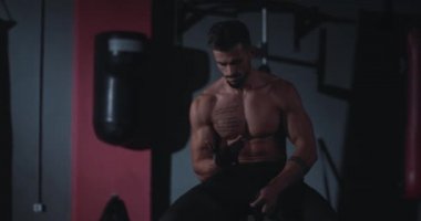Portre konsantre acımasız atletik adam jimnastik sınıfında sandalyede otururken profesyonel bandajlar kullanarak ellerini sarar