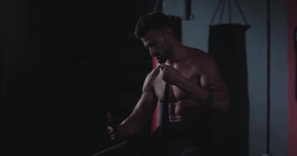 Симпатичный парень заворачивает руки черными бинтами на занятиях по фитнесу, готовясь к тренировкам — стоковое видео