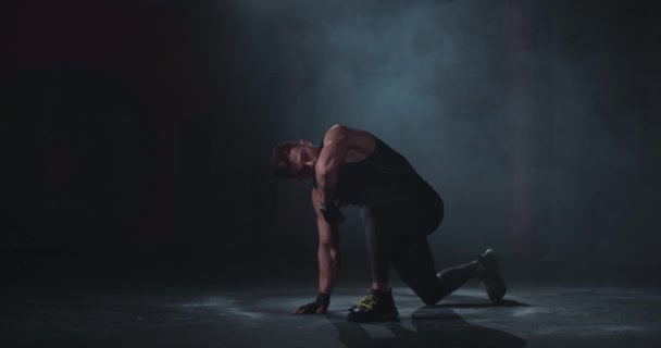 Поза бодибилдера показывает его мышцы в черной студии перед камерой в профессиональной спортивной одежде — стоковое видео