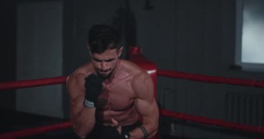 İyi görünümlü güçlü vücut adamı kameraya yakın durduğunda boks ringinde siyah boks eldiveni giyerek sıkı bir antrenman yapıyor.