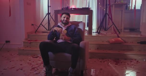 Smiling attractive guy at home party while drinking some drink and sitting on the sofa he chilling out — Stock Video