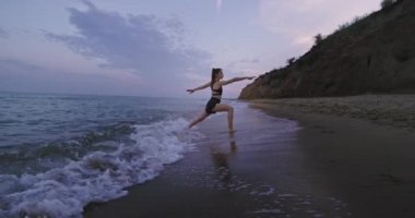 Spor kıyafetleriyle genç bir plaj manzarası. Suda ayakta dururken yoga meditasyonu yapıyor. Yavaş hareketler