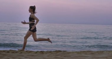 Sahilde koşan profesyonel bir bayan siyah bir spor giyim kuşamı giyerek sıkı koşuyor.