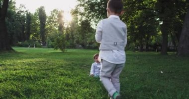 Takım elbiseli iki sevimli çocuk parkta bir topla çimenlerde oynuyorlar. Küçük çocuk ağlamaya başlıyor.