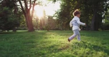 Beautiful charismatic boy in the suit running funny through the grass in the park smiling large in front of the camera