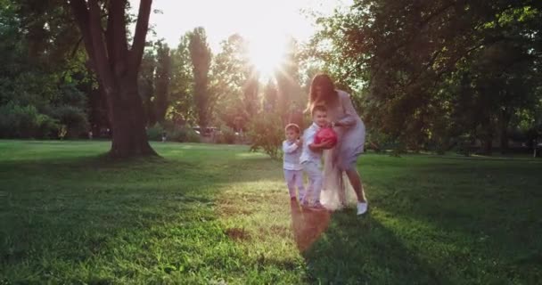 Corriendo feliz joven mami y su lindo dos niños pequeños en un traje elegante a través de la hierba verde sonriendo y sintiéndose feliz — Vídeo de stock
