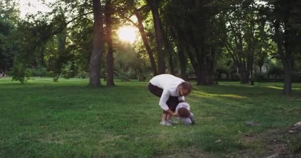 Jovem pai com seu filho pequeno aproveitando o tempo juntos brincando e se divertir no meio do parque — Vídeo de Stock