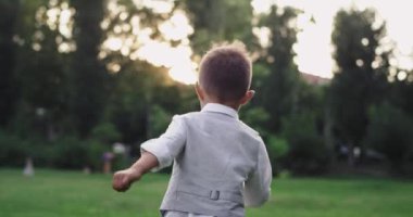 Little cute boy in a suit running through the green grass in the middle of the park enjoying the time at nature