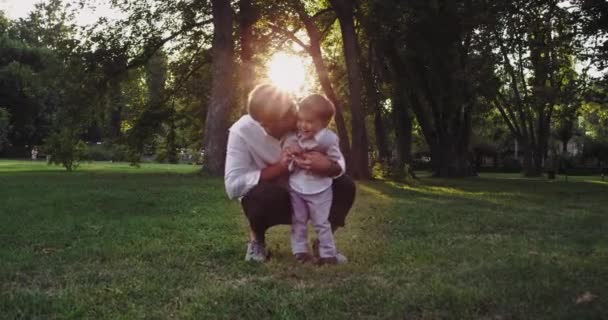 Papai jogando muito bonito com seus dois anos menino eles são muito elegante vestido apreciando o momento juntos no meio do parque — Vídeo de Stock