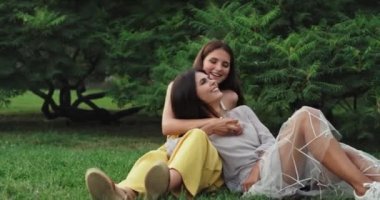 Yaz günü iki güzel bayan çimenlerin üzerinde birlikte eğleniyor gülümsüyor ve mutlu hissediyorlar.