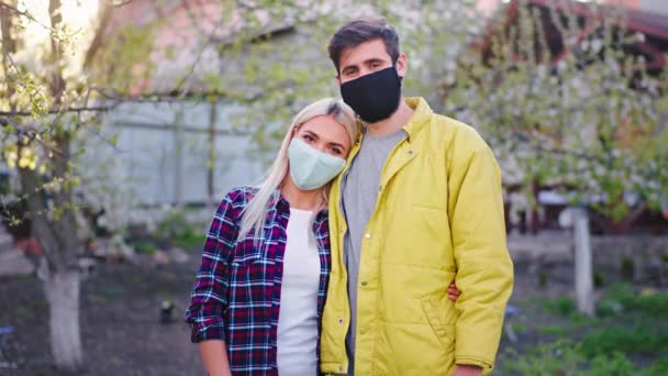 V přední části kamery v karanténě doma v zahradní paní a muž s ochrannou maskou objímající se navzájem hledí přímo do kamery — Stock video
