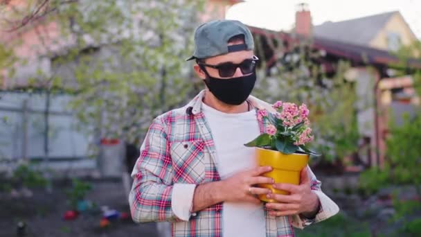 Na frente do homem da câmera com uma máscara protetora segurando um vaso de flores na quarentena do Coronavirus 2019 — Vídeo de Stock