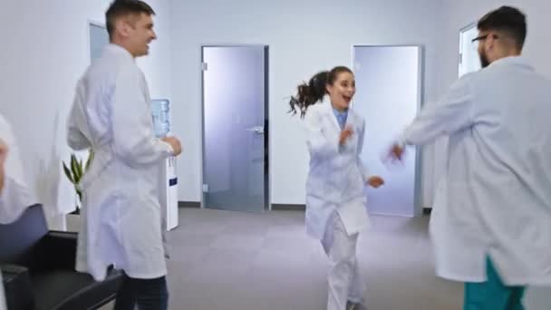 Sonriendo gran grupo de enfermeras y médicos bailando emocionados delante de la cámara en un moderno pasillo del hospital son muy divertidos. Disparo en ARRI Alexa Mini — Vídeos de Stock