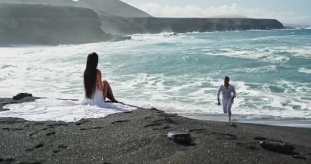 Mężczyzna i jego kobieta na plaży mają romantyczny czas wraz z niesamowitym widokiem krajobraz pięknej czarnej plaży i widok na morze. Zwolnione ruchy — Wideo stockowe