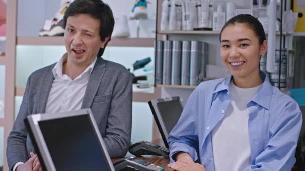 Devant l'appareil photo très heureux et souriant grand propriétaire homme de la boutique de chaussures et la jeune femme vendeur regardant vers l'appareil photo et montrant grand comme — Video