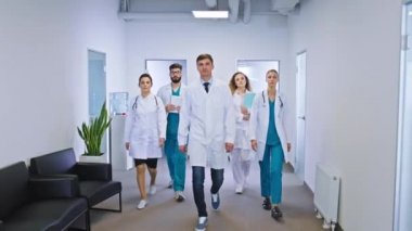 Modern bir hastane koridorunda kameranın önünde birlikte yürüyen çok ırklı bir grup doktor ve hemşire.