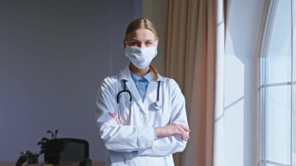 Krásná mladá žena lékař s ochrannou maskou si dává pauzu při pohledu přes panoramatické okno a myšlení. Shot na ARRI Alexa Mini — Stock video