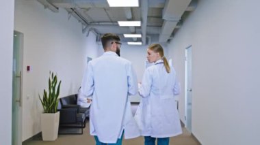 İki genç hemşire bayan ve adam hastane koridorunda yürüyorlar ve haritayı tutarken bazı sorunları tartışıyorlar diğer doktorlar sandalyede oturuyorlar.