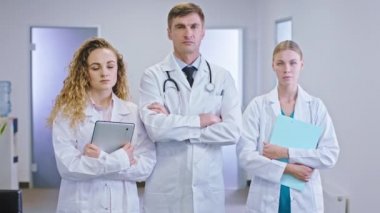 Olgun erkek doktor ve hemşire yardımcısı hastane koridorunun ortasında kameranın önünde dikilip dijital tablet ve harita tutuyorlar.