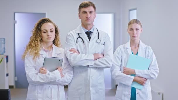 Uomo maturo medico e la sua assistenza infermiere in piedi di fronte alla telecamera nel mezzo del corridoio dell'ospedale e tenendo tablet digitale e mappa — Video Stock