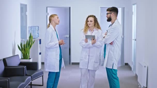 Médicos carismáticos dos mujeres y un hombre en el pasillo del hospital analizando el diagnóstico de la paciente y el tratamiento futuro — Vídeo de stock