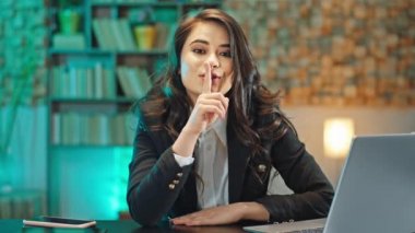 Karanlık ofis iş yerinde çekici genç bir kadın doğrudan kameraya bakıyor ve parmaklarıyla sessizlik içinde olduğunu gösteriyor. ARRI Alexa Mini 'de çekilen