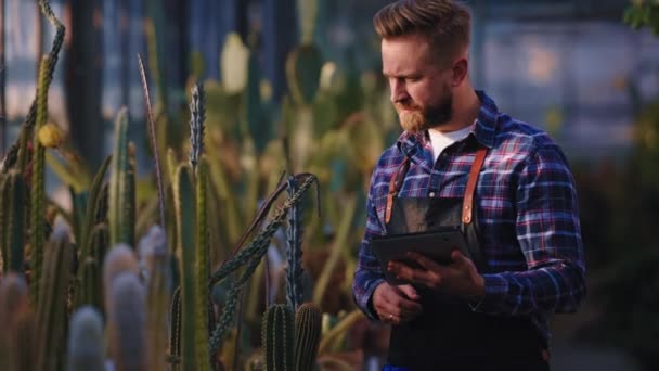 Konzentriert macht sich der charismatische Gärtner auf seinem elektronischen Tablet Notizen über den Zustand der Zierpflanzen. Schuss auf ARRI Alexa Mini — Stockvideo