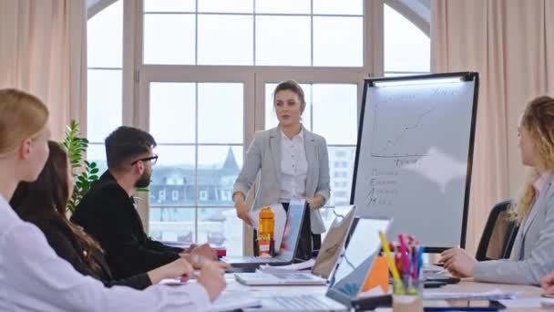 Modern konferans odasında olgun, güzel bir iş kadını meslektaşlarına bir eğitim sunumu semineri veriyor ve hep birlikte liderlik fikirlerini tartışıyor. — Stok video