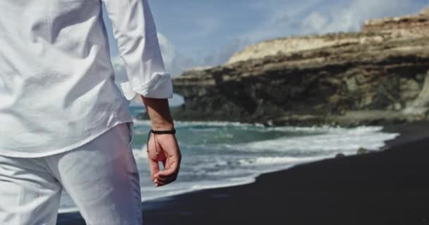 Paisaje captura de vídeo de un hombre caminando a través de la playa de arena negra junto al mar — Vídeos de Stock