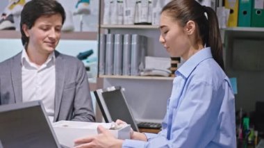 Gülümseyen mutlu satıcı genç Asyalı kadın müşteriyle tartışıyor ayakkabıları alıyor ve müşterinin kredi kartıyla ödemesi için terminali alıyor.