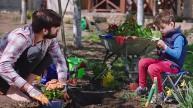 Bahçedeki adam ve oğlu bahçede çene çalarken bitkileri toprağa ekiyorlar ve birlikte vakit geçiriyorlar.