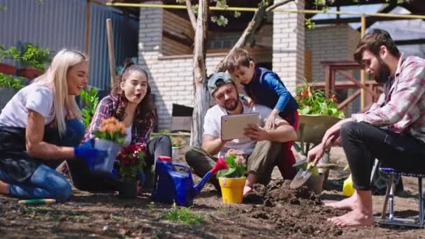 友人の大企業で幸せな時間彼らは庭で時間を楽しんで、より多くの植物や花を植えることで、より多くの情報を得るためにタブレットを取ります正しい植え方 — ストック動画