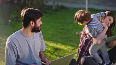 Bahçede gülümseyen anne ve baba sevimli oğullarıyla çimlerin üzerinde oynuyorlar. Aileyle eğleniyorlar.
