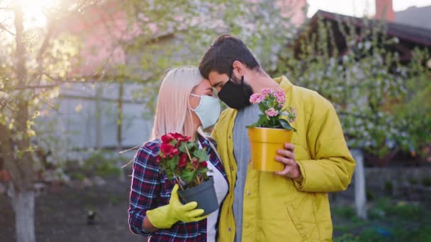 Upprörda par i trädgården hemma i karantänen framför kameran håller två blomkrukor de kramar varandra bär skyddsmask i pandemisk Coronavirus 2019. Skjuten på ARRI Alexa — Stockvideo