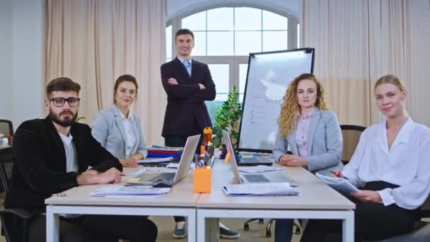 Attraktives Büroteam vor dem Teamleiter, der direkt in die Kamera blickt und groß lächelt, sie sitzen in ihrem Konferenzraum — Stockvideo