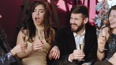 Kameranın önünde karizmatik bir grup öğrenci Noel partisini kutlarken kanepede oturup sosyalleşiyorlar ve biraz köpüklü şarap içiyorlar.